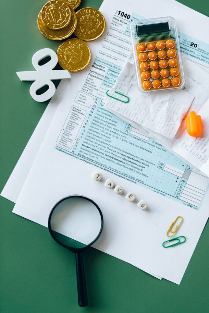 Top view of tax forms, calculator, coins, and office supplies on a green desk.