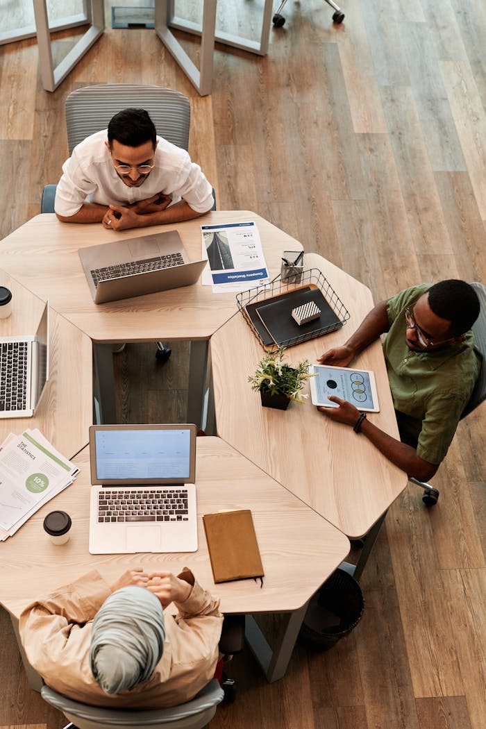 Top view of diverse team engaged in discussion with laptops and digital devices in modern office setting.